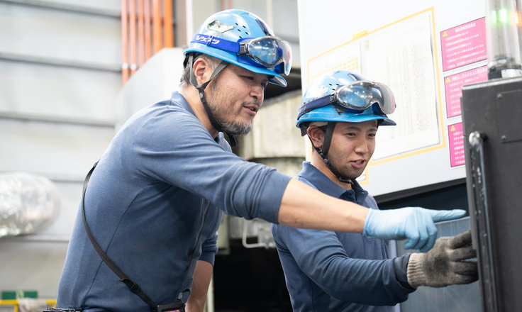 機械の前で後進を指導する社員